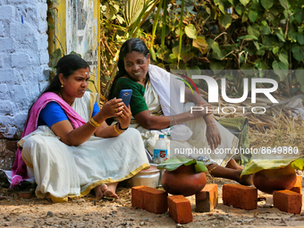 Hindu women look at a phone for updates from the Attukal Temple website as to when they can begin cooking pongala along the roadside on the...