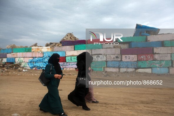  Palestinian women walk during a windy day  next a big stone wall on Oct. 25, 2015. that was painted by local artists at the sea port in Gaz...