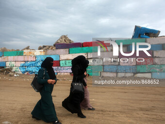  Palestinian women walk during a windy day  next a big stone wall on Oct. 25, 2015. that was painted by local artists at the sea port in Gaz...