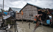 A man washes his cloth while his house is almost submerged by the water of high tide at Ka...