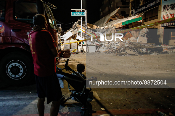 A man with a boy in a pram surveys the wreckage of a collapsed residential building after a magnitude 6.8 earthquake strikes Taiwan, in Yuli...