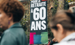 Demonstrators walk in front of a large banner hanging demanding the introduction of the 60...