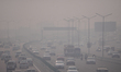 Traffic moves along a highway shrouded in a thick layer of smog and haze in New Delhi, Ind...