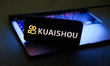 Kuaishou logo displayed on a phone screen and a laptop are seen in this illustration photo...