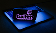 Twitch logo displayed on a phone screen and a laptop are seen in this illustration photo t...