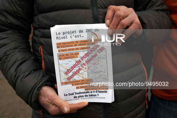 A man shows a flyer reading 'The Rivel's project is 110ha less of agricultural fields and 80ha more of concrete, two times more trucks and m...