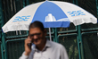 A man talks on phone walks past an umbrella written BSE (Bombay Stock Exchange) near Dalal...