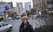 A young Iranian woman wearing a hat looks on while standing on a street-side in northern T...