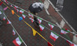 An Iranian man carrying an umbrella walks under Iran flags in downtown Tehran on the eve o...