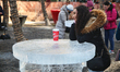 Woman poses for a photo by a table made of solid ice at an outdoor cafe during Icefest in...
