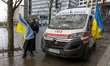 A woman from Ukraine poses with the Ukrainian flag in front of the ambulance. Ambulance hi...