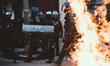 Riot police march behind a lit garbage can fire after clashes with thugs and black blocs a...
