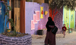  Palestinians walk past the facades of houses painted by artists in Gaza City, on March 11...