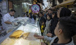 Iranian people wait to receive traditional breads while shopping from a vendor at a local...