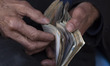 An Iranian vendor counts Iranian banknotes while sitting at a local outdoor bazaar (Market...