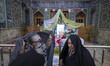Veiled Iranian women stand in front of a Haft-seen (Seven S) table decorated in a holy shr...