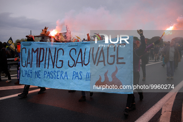 Protesters use flares while holding a banner reading 'Wild camping, the A69 won't be'. More than 8000 protesters marched 12km against the pl...
