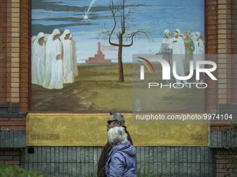 A couple walks under a representative painting about the Chernobyl accident in the walls of the Chernobyl church in Kyiv, on april 26, 2023,...